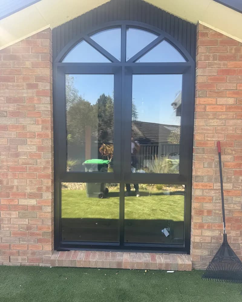 Tall black aluminium window with an arched top, set into a red brick gable wall