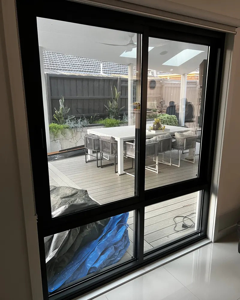 Black aluminium sliding window seen from inside, looking out to a covered deck with an outdoor table